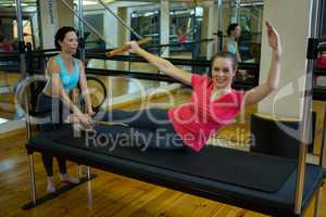 Female trainer assisting woman with stretching exercise on reformer