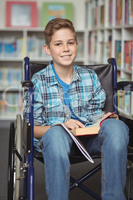 Portrait of disabled schoolboy holding book in library