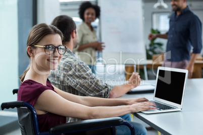 Portrait of smiling business executive in wheelchair working on laptop in meeting