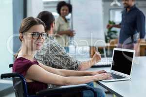 Portrait of smiling business executive in wheelchair working on laptop in meeting