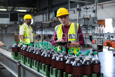 Factory worker with digital tablet monitoring drinks production line