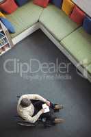 Overhead view of disabled school teacher using digital tablet in library