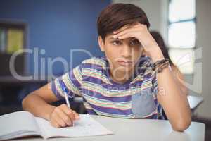 Tensed school boy doing homework in classroom