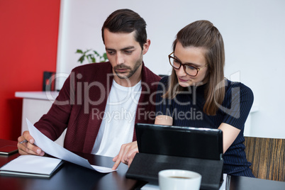 Two business executives discussing over digital tablet and document in meeting