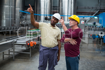 Two factory workers pointing upwards while discussing together