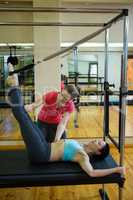 Female trainer assisting woman with stretching exercise on reformer