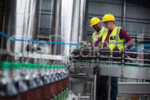 Factory workers monitoring cold drink bottles at drinks production plant