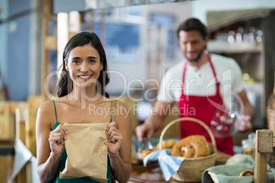 Portrait of smiling female customer showing parcel bag at counter