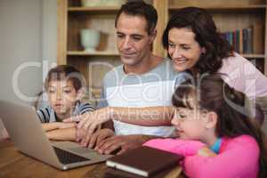 Parents and kids using laptop on table in study room