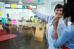 Female graphic designer pointing to the sticky notes on the glass in creative office