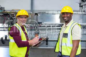 Portrait of two factory workers with clipboard standing next to production line