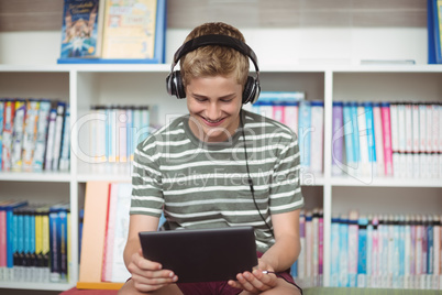 Happy schoolboy listening music while using digital tablet in library