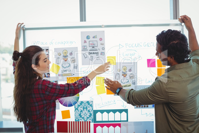 Male and female graphic designers discussing over sticky notes