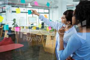 Female graphic designer pointing to the sticky notes on the glass in creative office