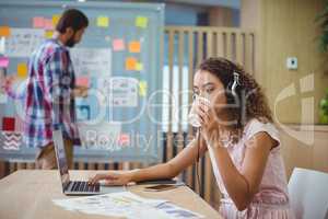 Female graphic designer drinking coffee while using laptop