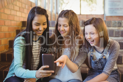 Smiling schoolgirls sitting on the staircase using mobile phone