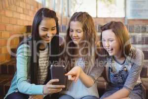 Smiling schoolgirls sitting on the staircase using mobile phone
