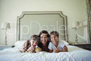 Mother and kids lying on bed with teddy bear in bedroom