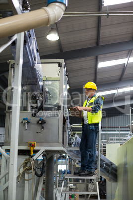 Male factory worker maintaining record on clipboard