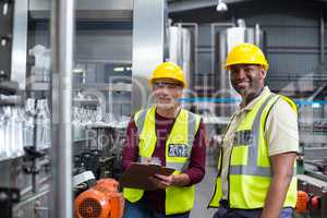 Two factory workers discussing while monitoring drinks production line