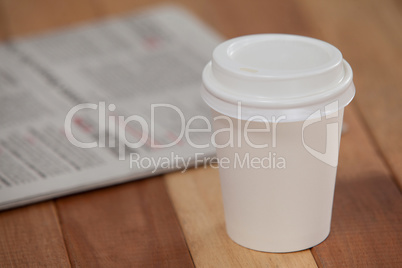 Close-up of disposable coffee cup and newspaper