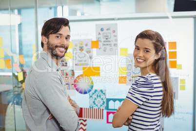 Portrait of male and female business executives standing with arms crossed near whiteboard