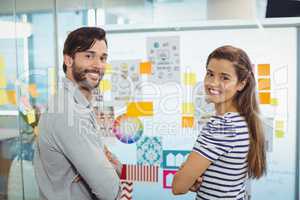 Portrait of male and female business executives standing with arms crossed near whiteboard