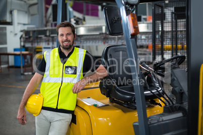 Portrait of smiling factory worker leaning on forklift