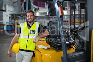 Portrait of smiling factory worker leaning on forklift