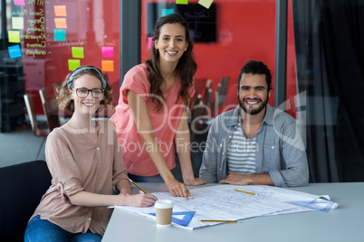 Portrait of smiling business executives with blueprint on table