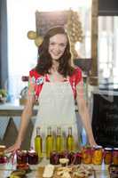 Female shop assistant standing at the counter with pickle, olive oil and jam bottles