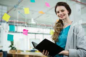 Smiling female executive standing with folder in creative office