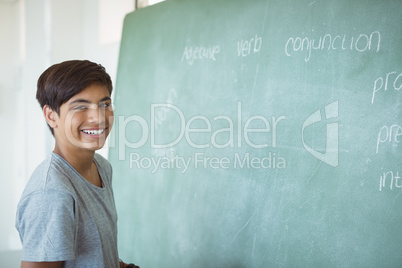 Portrait of smiling schoolboy standing near chalkboard in classroom