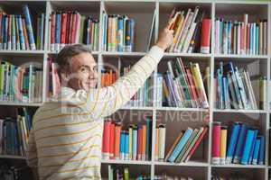 Portrait of happy school teacher selecting book in library