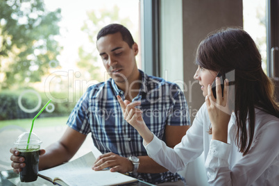 Executives talking on mobile phone while discussing on diary