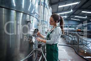 Female factory worker turning control wheel of storage tank