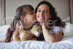 Daughter kissing her mother on cheek in bedroom