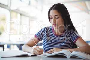 Attentive schoolgirl doing homework in classroom