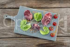 Sirloin steak, cherry tomatoes and cabbage leaves on board against wooden background