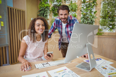 Portrait of executives smiling at desk while working on personal computer