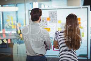 Male and female business executives looking at whiteboard in office