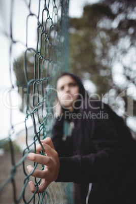 Anxious teenage girl leaning on wire mesh fence