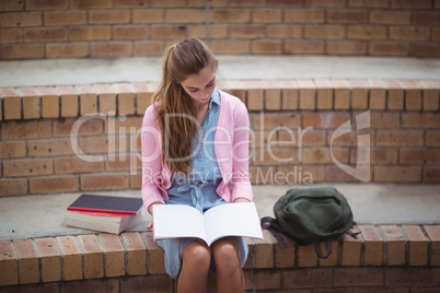 Attentive schoolgirl reading book in campus