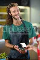 Smiling male staff receiving a payment through nfc technology at counter