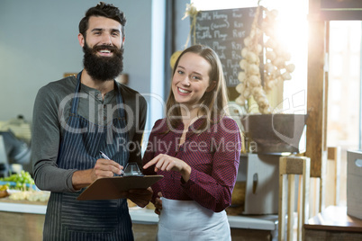 Portrait of smiling bakery staff writing on clipboard at counter