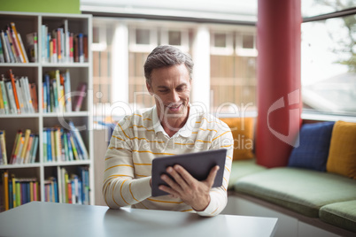 Attentive school teacher using digital tablet in library