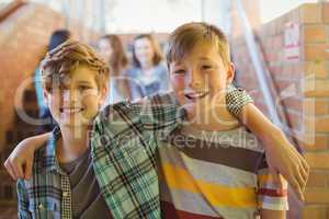 Portrait of smiling schoolboys standing with arm around in corridor