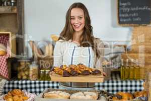 Portrait of smiling female staff holding a wooden tray of dessert at counter