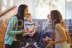 Happy two schoolgirls interacting with each other in corridor