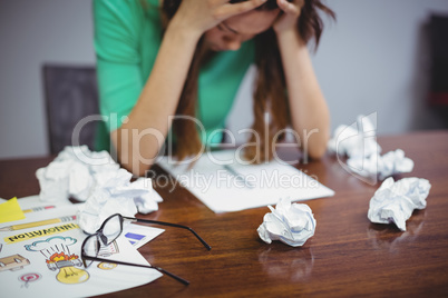 Frustrated female business executive sitting with crumpled papers balls